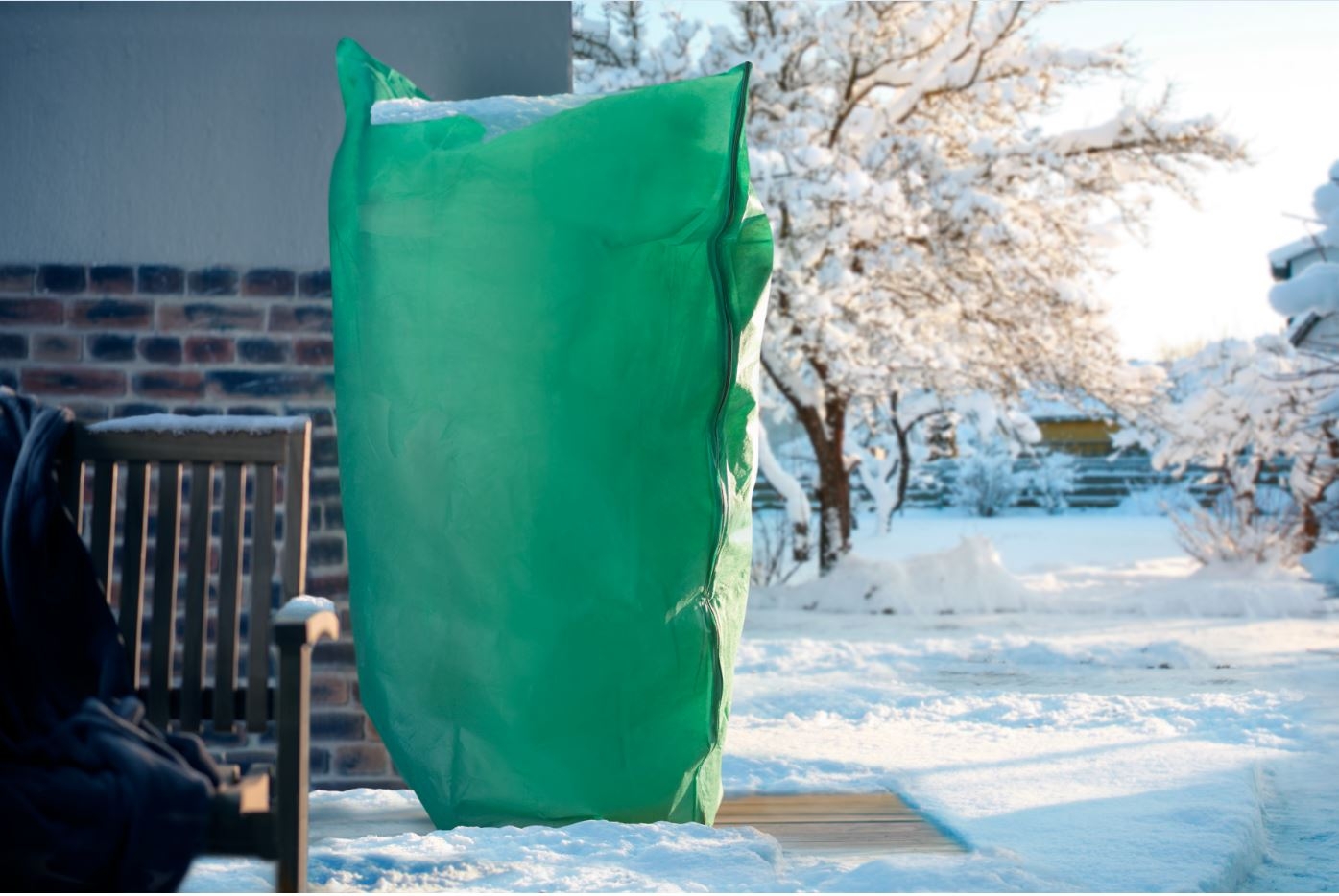 Een groene winterbeschermhoes bedekt een plant in een besneeuwde tuin.